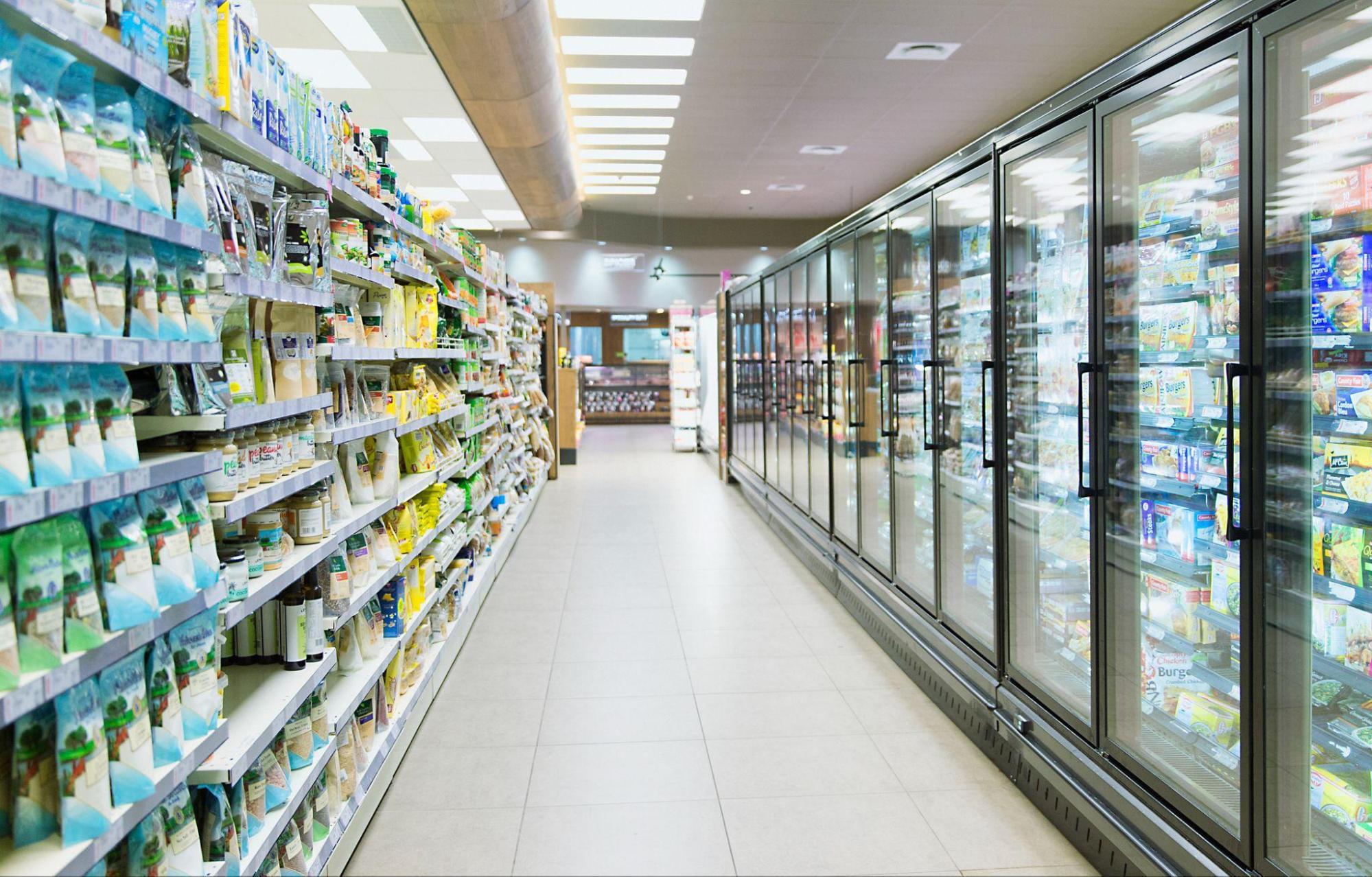 A grocery store aisle showing a frozen food section on the right and shelves of products on the left.
