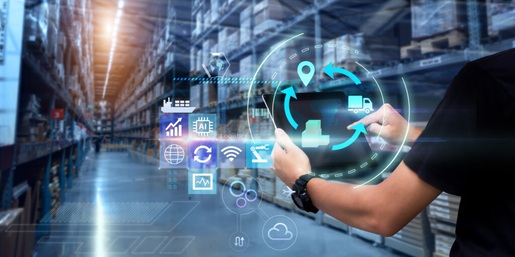 Supply chain concept with a man using a tablet with a blurred background of the inside of a warehouse with technology symbols appearing in the mid-ground.