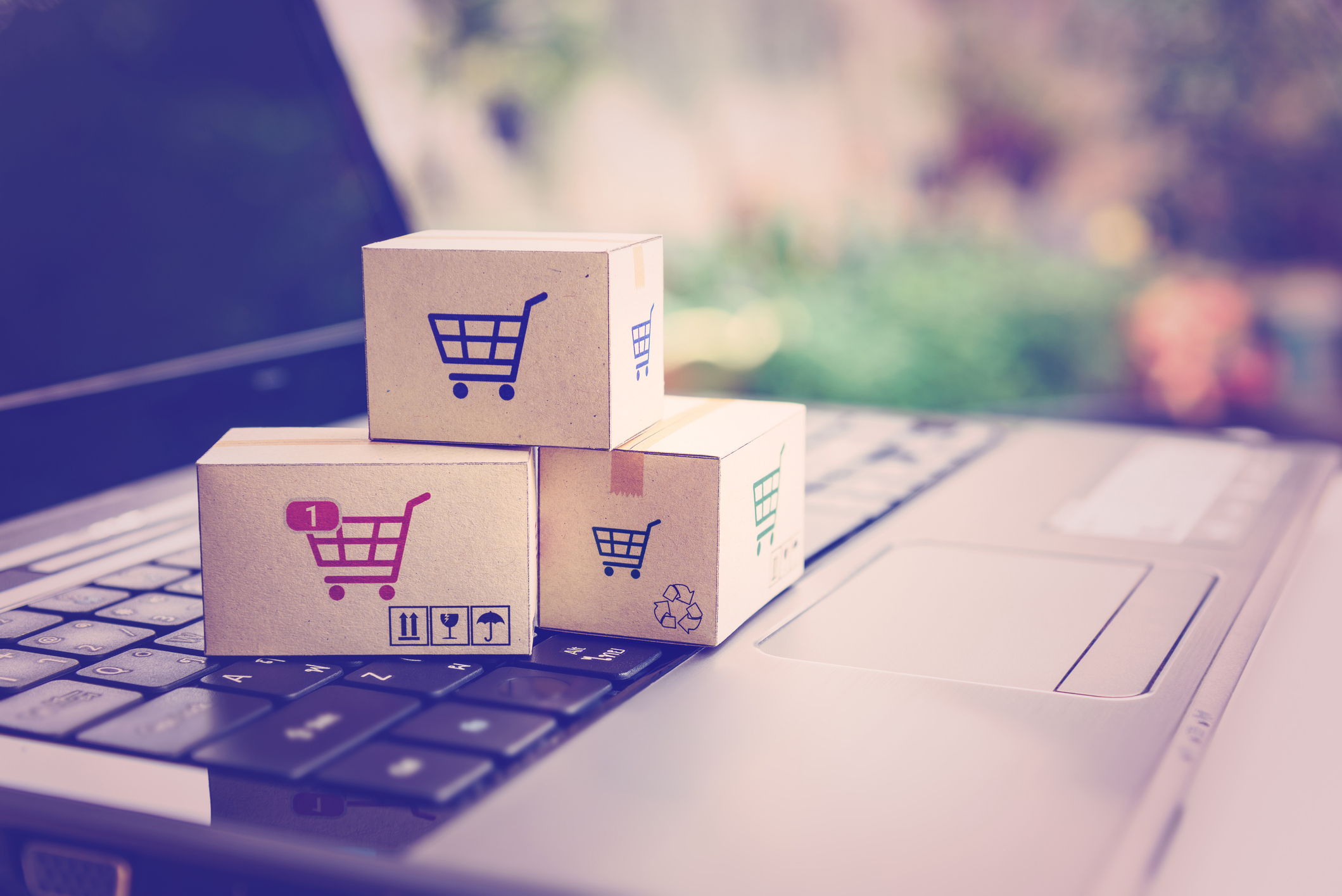 Paper cartons with a shopping cart or trolley logo on a laptop keyboard. Conveys the idea of customers ordering from retailer sites via the internet.