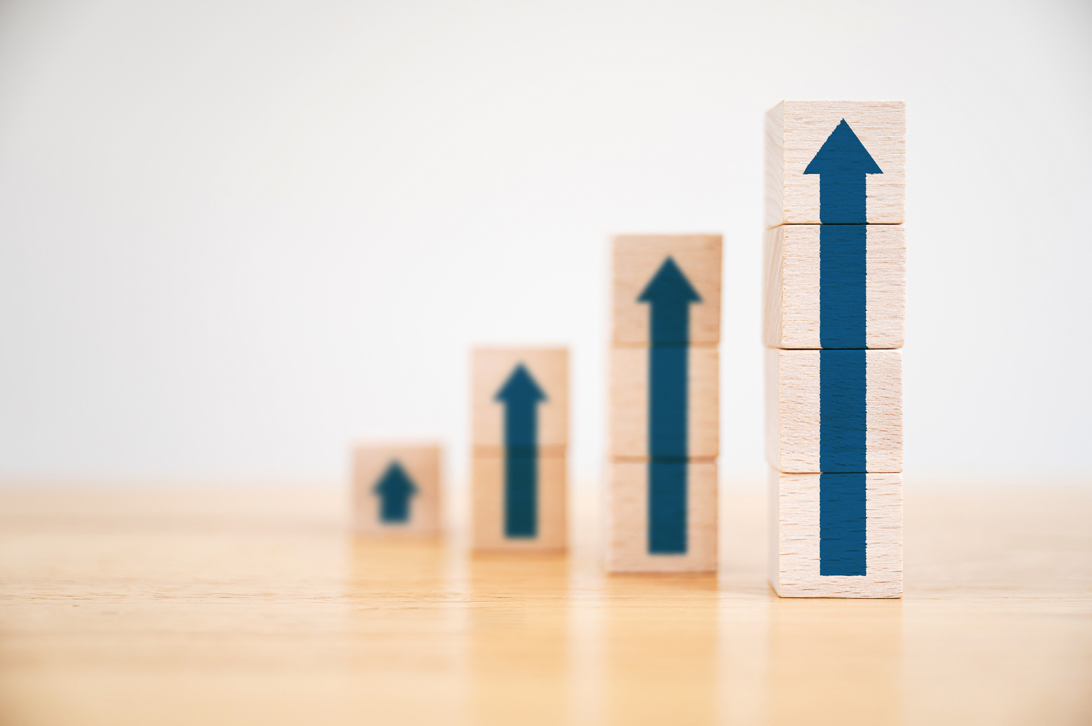 Wooden blocks increasingly stacking as step stair with blue arrows pointing up on each stack.